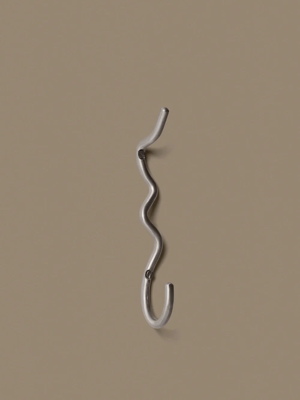 Ferm Living Curvature Hook in black, minimalist metal wall hook for accessories, mounted on a white wall.
