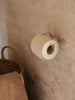 Ferm Living Curvature toilet paper holder in matte black mounted on bathroom wall with a roll of toilet paper.