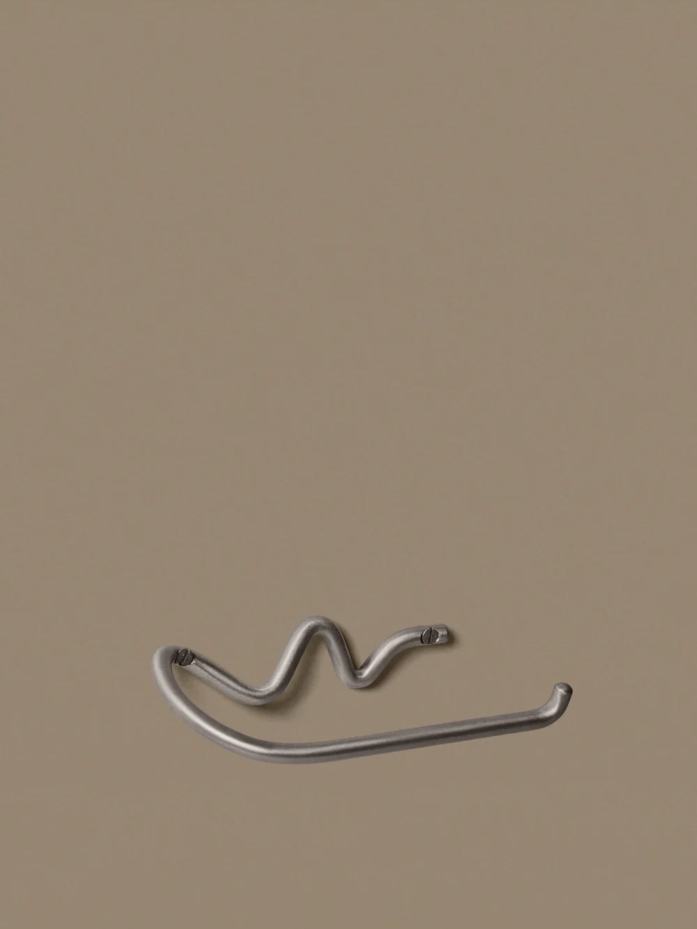 Ferm Living Curvature toilet paper holder in modern black metal, mounted on a bathroom wall for convenient use.