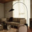 Ferm Living Arum arched floor lamp with sleek black metal arc and minimalist design, standing on a wooden floor.