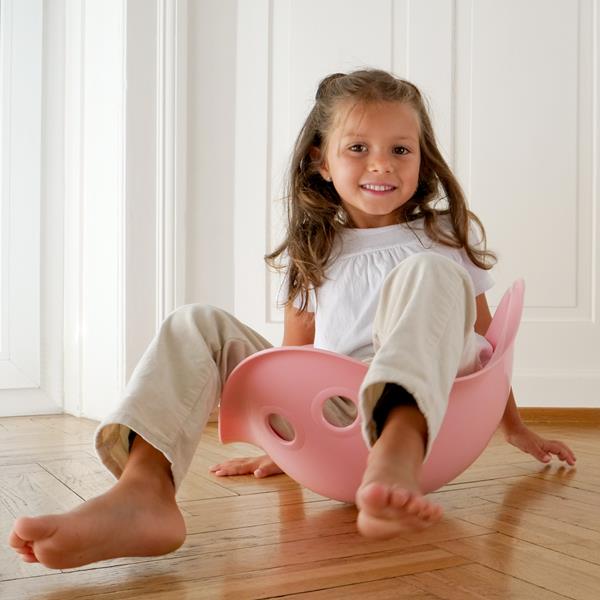 Kids playing with a pink Moluk Bilibo plastic toy in a colorful indoor setting.