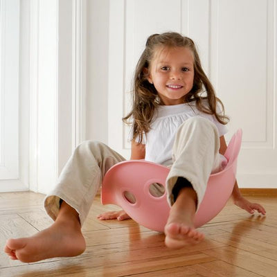 Kids playing with a pink Moluk Bilibo plastic toy in a colorful indoor setting.