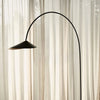 Ferm Living Arum Arched Floor Lamp with sleek metal arch and modern lighting design, standing tall in a contemporary interior setting.