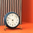 Arne Jacobsen Station Table Clock resting on a wooden surface, showcasing a sleek, minimalist design in natural light.