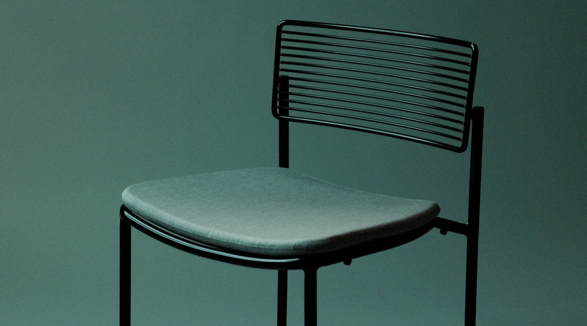 The Rachel Chair by Bend Goods, a stylish modern seating with a curved metal frame and woven seat, designed for contemporary interiors.