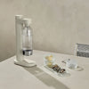 Stelton Brus Carbonator accessory in soft sand color, designed for sparkling water bottles, with a sleek modern look.