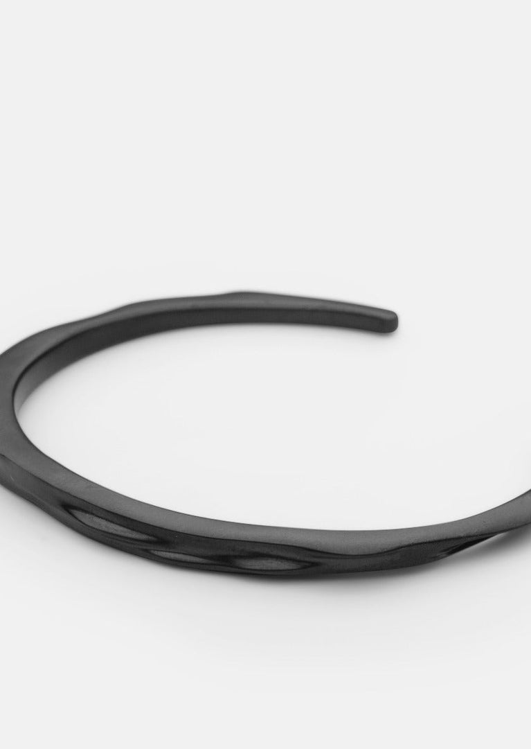 Skultuna Titanium Black Opaque Objects Cuff bracelet in matte black metal, shown from an angled view on a white background.