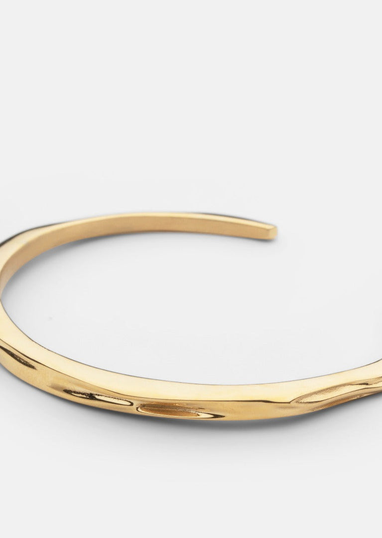 Gold plated Opaque Objects Cuff bracelet by Skultuna, shown from an angle highlighting its shiny, smooth surface and modern design.