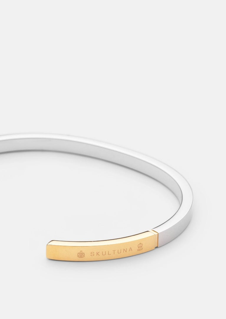 Skultuna SB Cuff Thin in two-tone steel and gold, showcasing a sleek, minimalist accessory with a polished finish.